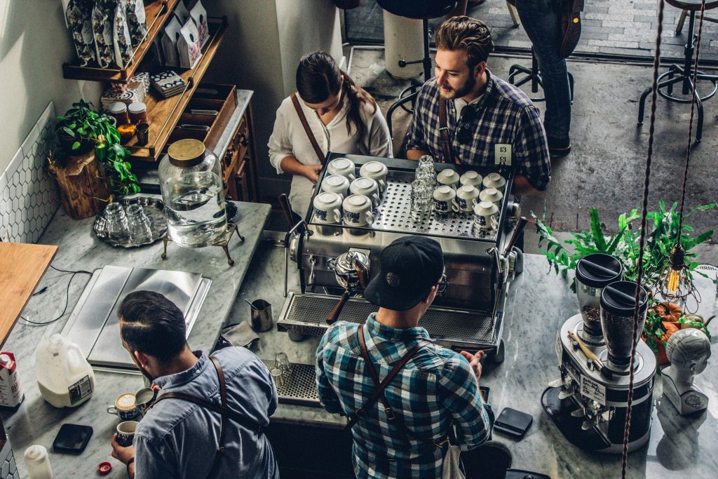 a group of people standing around a small business counter with coffee machines